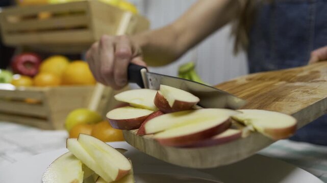 Slow motion of woman using knife to push apple slices off cutting board and onto plate - closeup