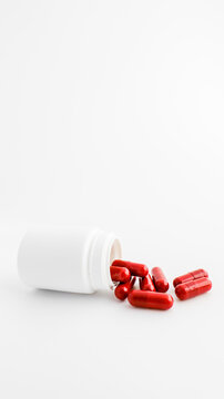 Red medicinal capsules spilling out of a white bottle on a clean white background