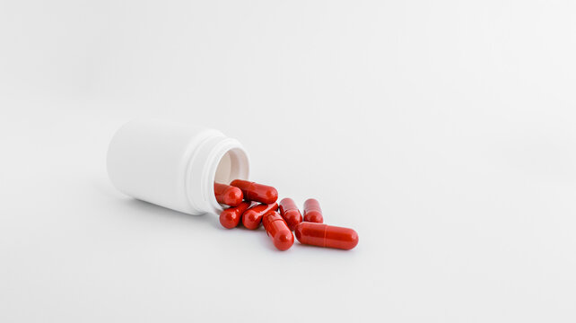 Red capsules spilling out of a white prescription bottle on a clean white background