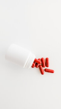 Red capsules spilling out of a white pill bottle on a clean white background