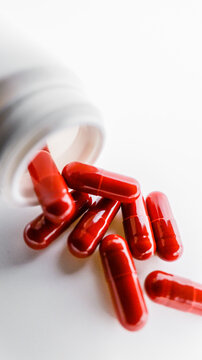 Red medicinal capsules spilling out of a white bottle onto a clean white surface