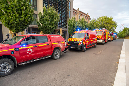 Convoy of red emergency and rescue vehicles parked along an urban street in France. pompiers