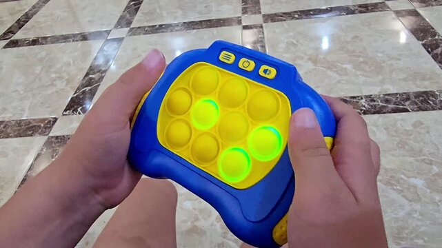 Child playing with an electronic pop it game, pressing illuminated bubbles and improving reaction, focus and hand coordination through interactive sensory play and entertainment