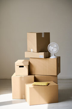 Vertical shot of stacked cardboard boxes, storage bin, parcel envelope, small fan, suggesting home relocation, packing, delivery logistics. Ideal for moving services, storage ads, ecommerce