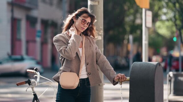 Video of tired woman cooling off with water from a drinking fountain after cycling through the city
