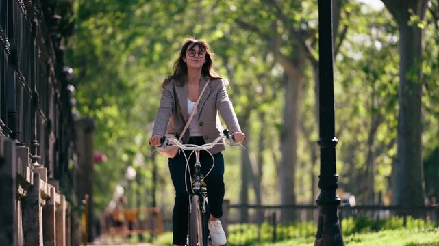 Video of smiling woman riding a bicycle through the park.