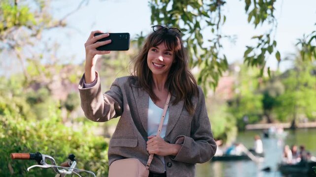 Video of pretty woman taking selfies with smartphone near the lake in the park