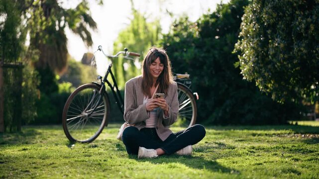 Video of pretty woman using her smartphone while resting after cycling in the park.