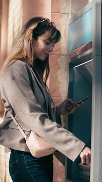 Video of beautiful woman withdrawing cash from an ATM using her smartphone in the city.