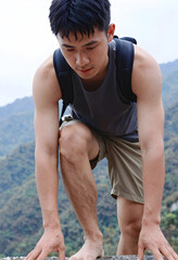 Fototapeta premium Young asian man with backpack climbing barefoot on a mountain trail, adventure and outdoor activity