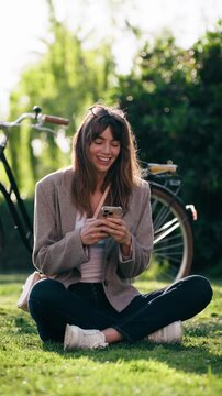 Video of pretty woman using her smartphone while resting after cycling in the park.