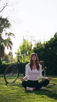 Video of pretty woman doing ioga while resting after cycling in the park.