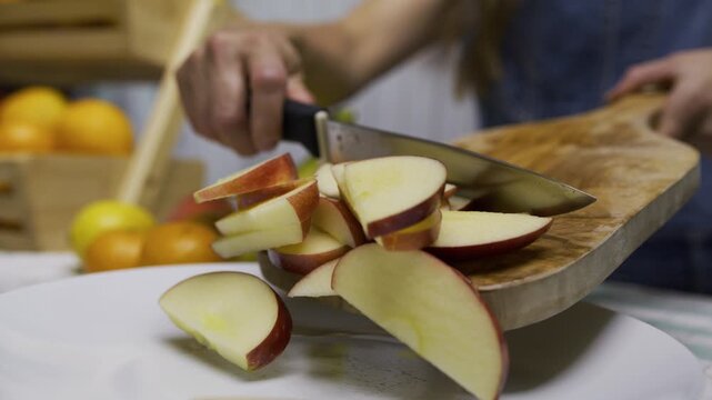 Cinematic slow motion of woman using knife to scrape apple slices off wooden board and onto plate, closeup