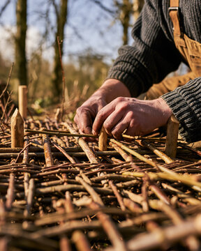 Hands weaving natural fibers in outdoor workshop, traditional artisan craftsmanship with woodwork and basketry pattern