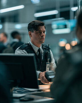 Airport security officer at service desk monitoring passenger IDs with scanner in modern terminal busy queue