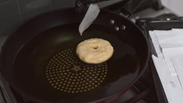 A baker deep-frying a donut in a pan full of hot oil in a bakery kitchen in Bangkok, Thailand