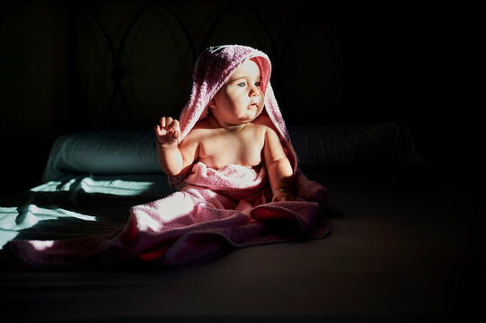 Baby wrapped in pink towel sitting on bed