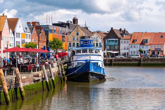 Historic harbor of Husum with an ship, waterfront restaurants and colorful old town beneath dramatic clouds on Germany's North Sea coast.