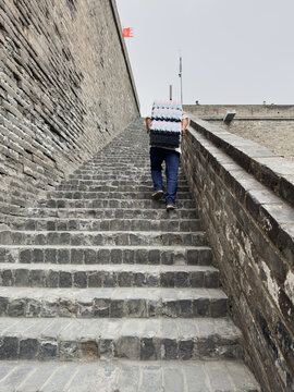 Worker carrying water bottles up Changle Gate city wall steps in Xian China by day
