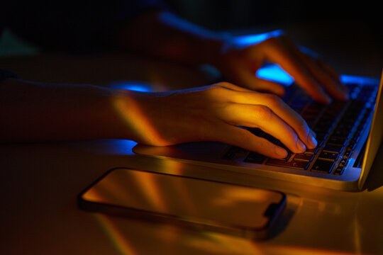 Neon hi-tech typing on laptop with smartphone in cyberspace
