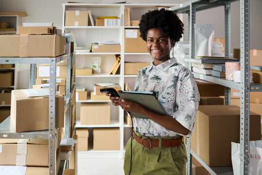 Portrait of young Black woman scanning inventory with barcode reader and tablet in warehouse, managing stock control and order fulfillment. Ideal for ecommerce logistics and retail operations