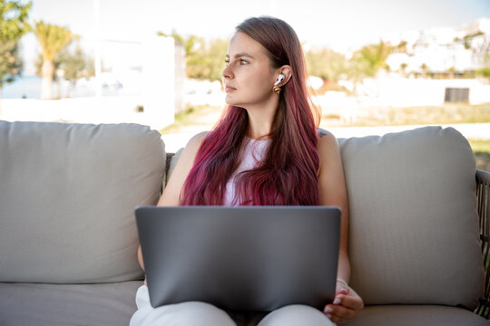 Young woman with laptop and earbuds on outdoor sofa