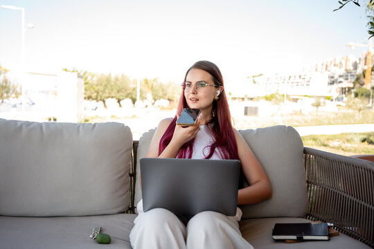 Young woman using voice message on phone with laptop outdoors