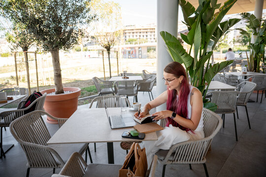 Woman working on laptop and notebook at outdoor cafe