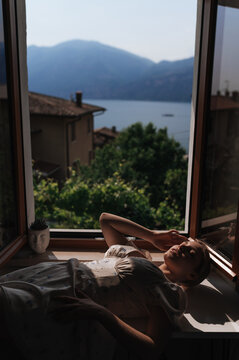 Woman resting by open window overlooking Lake Garda view