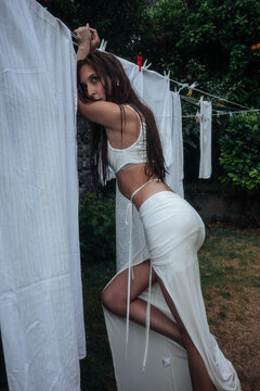 Young woman in white dress posing by outdoor laundry line