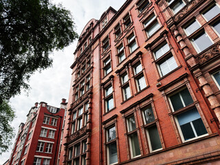 Fototapeta premium Historic red brick building facade in Manchester UK with ornate Victorian architecture and tall windows on a cloudy day