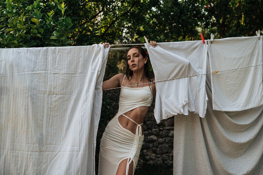 Young woman in white dress posing on outdoor clothesline