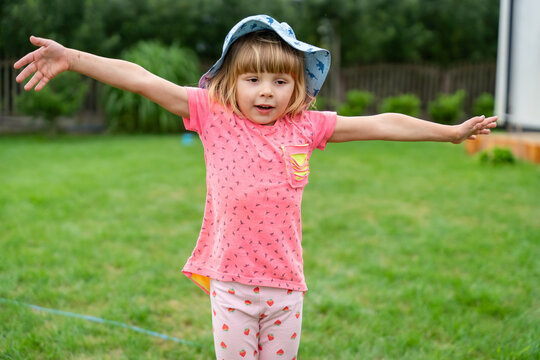 Little Girl Balancing With Outstretched Arms In Garden During Summer Outdoor Play