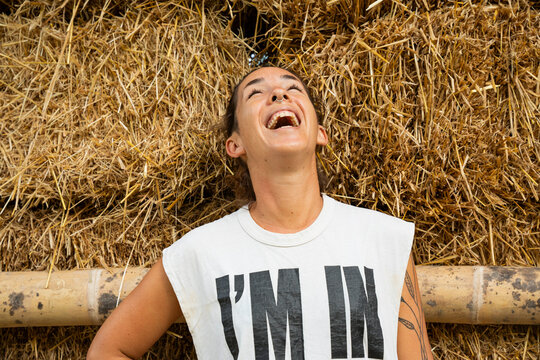 Happy woman laughing on straw bales at natural building site