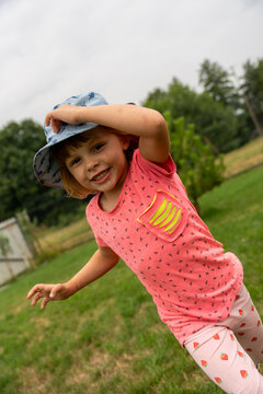 Smiling Little Girl Running In Garden Wearing Sun Hat During Summer Outdoor Play