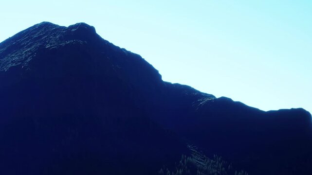 A dark mountain shape contrasts with a light blue sky. The mountain stands tall in a natural landscape. The scene shows clear weather and daylight.