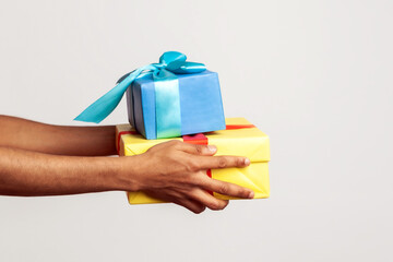 Profile portrait happy afro-american bearded guy with dreadlocks and in santa claus hat holding present boxes, preparing gifts on christmas and new year. Indoor studio shot isolated on gray background © khosrork