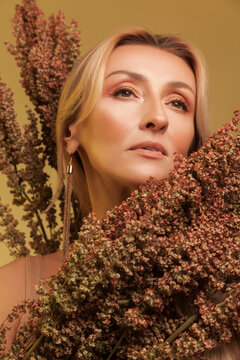 Graceful blonde woman looking up surrounded by dried sorghum plants isolated over yellow studio background