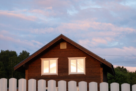 Cozy wooden cottage facade with white fence at dusk