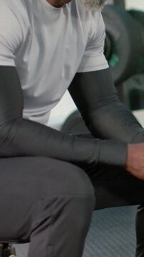 Vertical video: Pulling back showing man on gym bench turning, smiling, holding towel in gray tee
