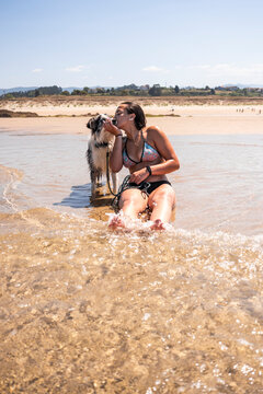 Woman kissing her dog in shallow water at sandy beach