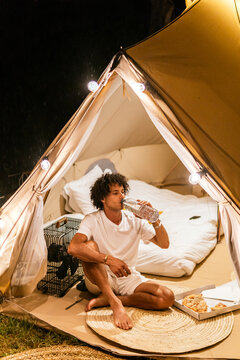 Man camping alone in glamping tent at night, relaxing