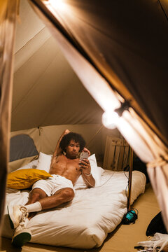 Man relaxing alone in tent at night using smartphone