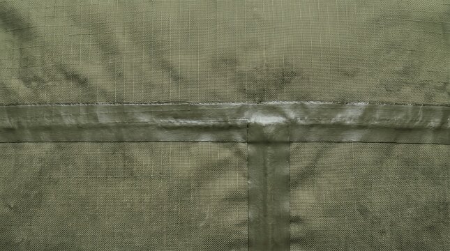 Olive green canvas fabric texture with stitched seams and waterproof tape detail close up showing rugged woven pattern and subtle weathered marks