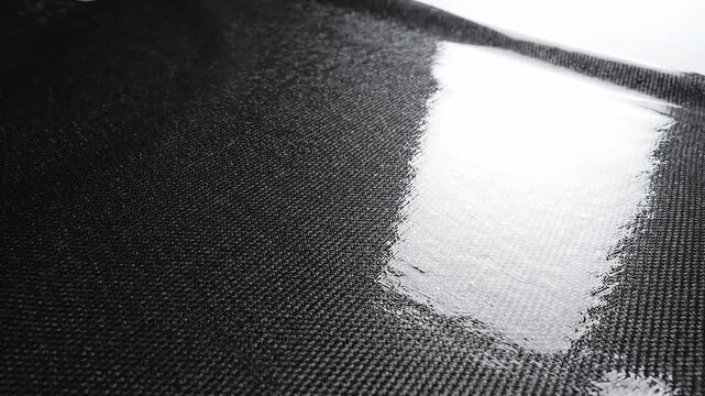 Carbon fiber sheet with glossy resin finish. Industrial composite material texture showing reflective woven pattern. Durable automotive and aerospace construction part.