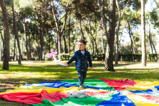 Child playing with balloon twisting on colorful parachute