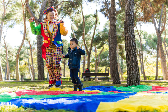 Clown leading child on parachute game in forest park