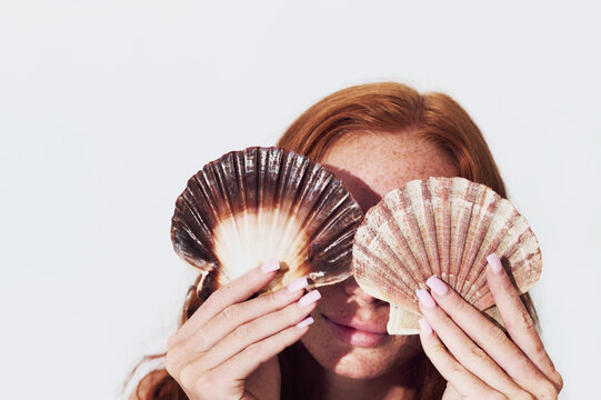 Woman playfully holding seashells by the poolside
