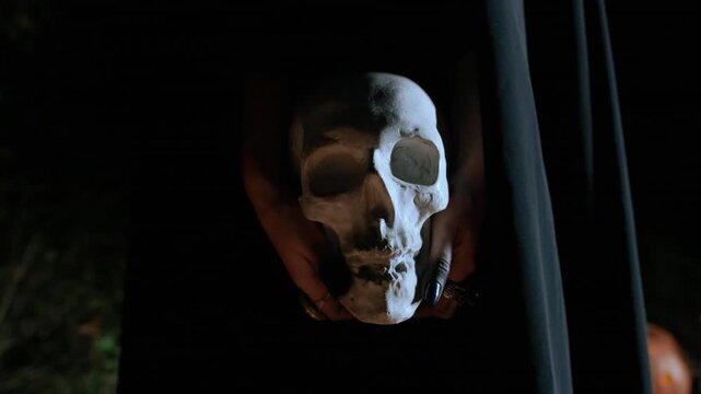 Hands cradle and present human skull in dark moody closeup, with cool side light, strong contrast, visible bone texture, cracked surface, and tense gothic atmosphere, with skull, hand, bone, closeup