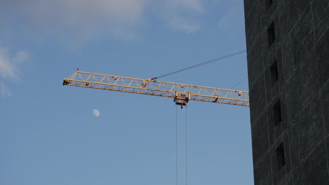 A tall construction crane is seen working under a clear blue sky